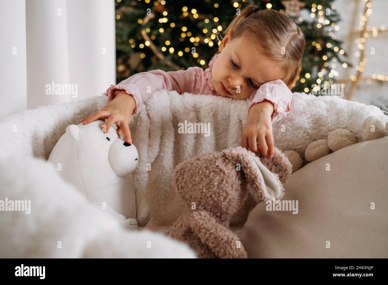 Nettes Kleinkind Kind wartet auf Geschenke zu Hause nach der Dekoration Weihnachtsbaum im Öko-Stil mit Holzspielzeug. Weihnachtsabend für Kinder. Nordischer Stil Stockfoto