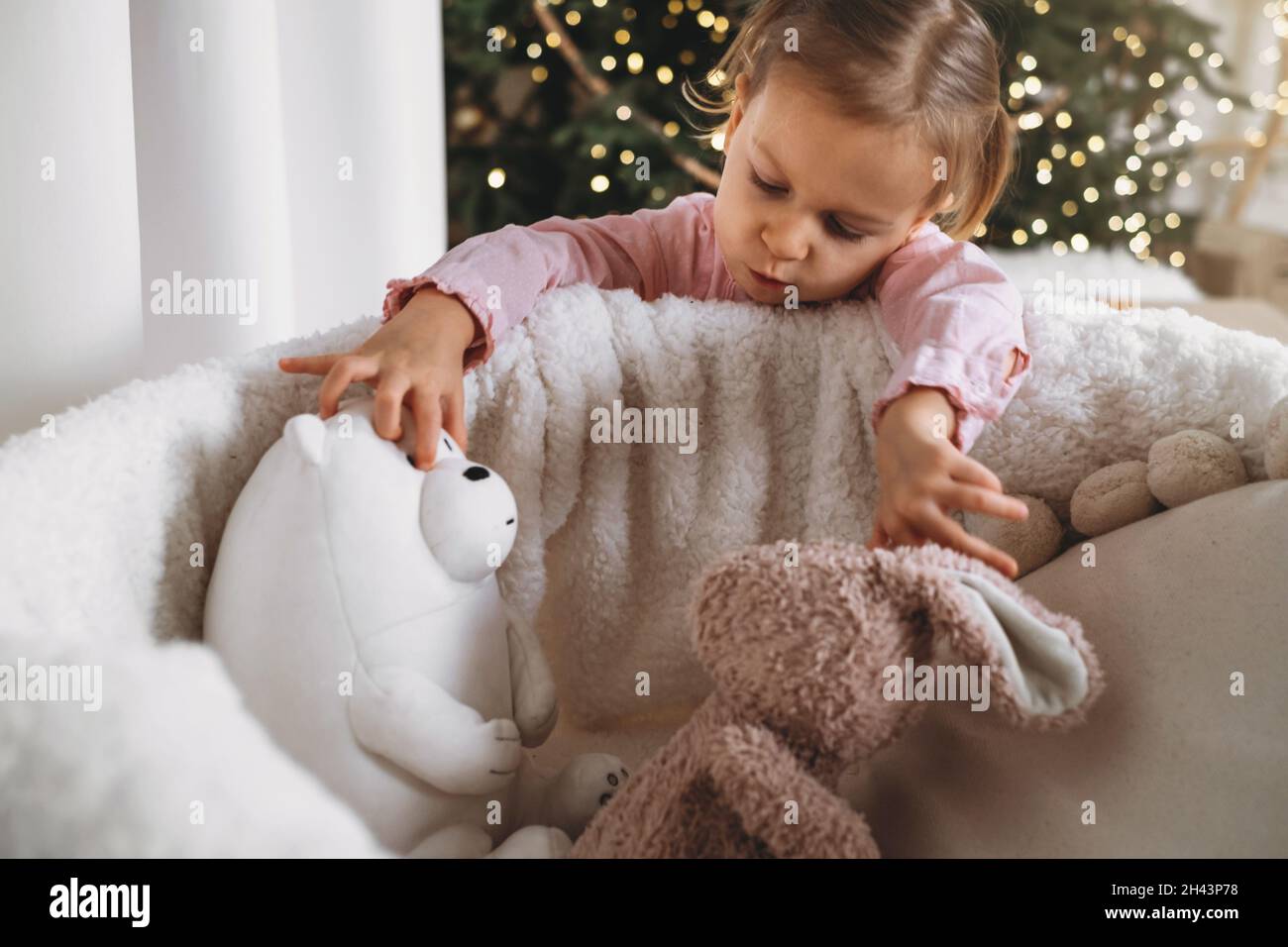 Nettes Kleinkind Kind wartet auf Geschenke zu Hause nach der Dekoration Weihnachtsbaum im Öko-Stil mit Holzspielzeug. Weihnachtsabend für Kinder. Nordischer Stil Stockfoto