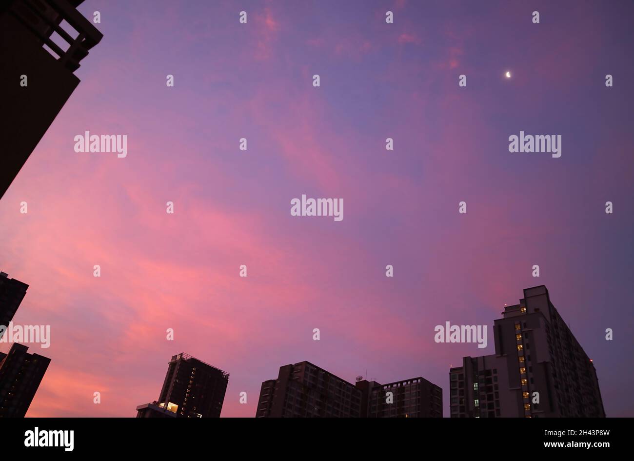Fantastischer Sonnenuntergang Himmel über der Stadt mit einem hellen Viertelmond Stockfoto