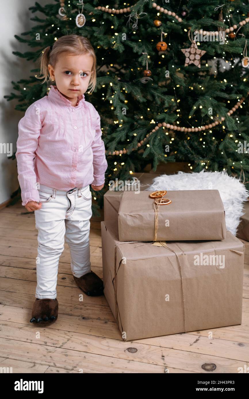 Nettes Kleinkind Kind wartet auf Geschenke zu Hause nach der Dekoration Weihnachtsbaum im Öko-Stil mit Holzspielzeug. Weihnachtsabend für Kinder. Nordischer Stil Stockfoto