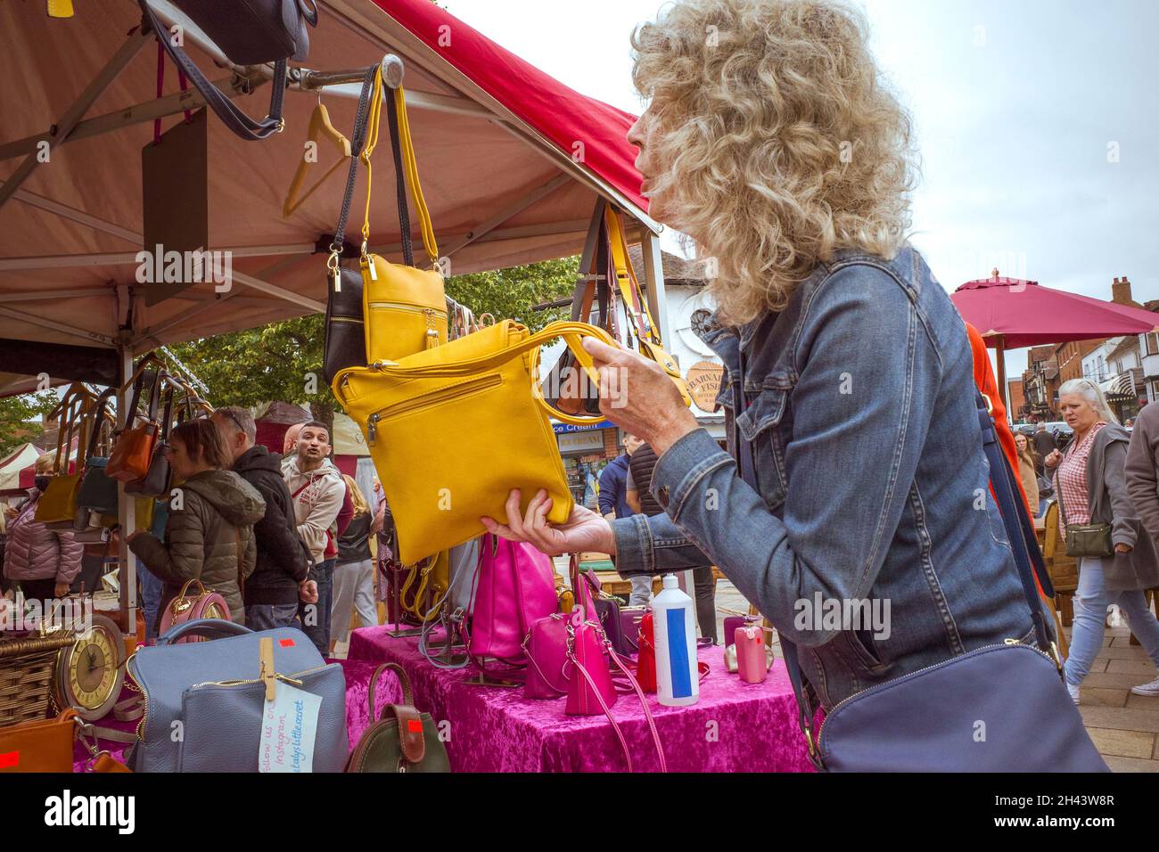 Eine Frau an einem Marktstand fragt nach dem Preis einer Handtasche, die ihr gefällt. Stockfoto