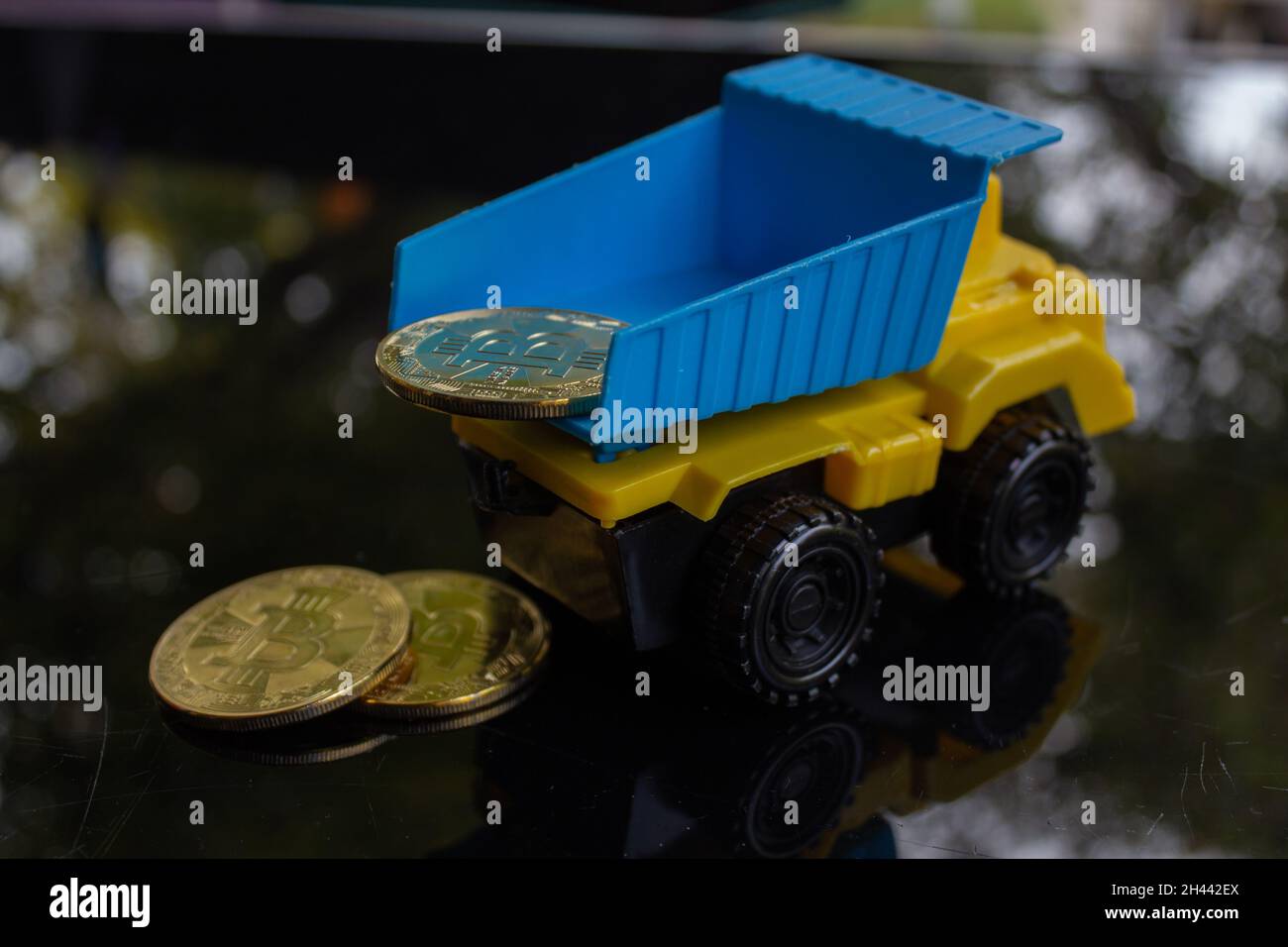 Ein gelber, türkisfarbener Spielzeugtruck, der einige Bitcoins trägt und ablegt. Stockfoto