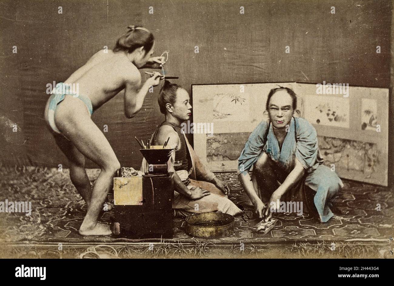 Japan: Ein Friseur mit Lendenschurz bei der Arbeit an einem knieenden Mann; ein Mann in einer Robe hockt vor ihm. Farbfoto, 1870/1890. Stockfoto