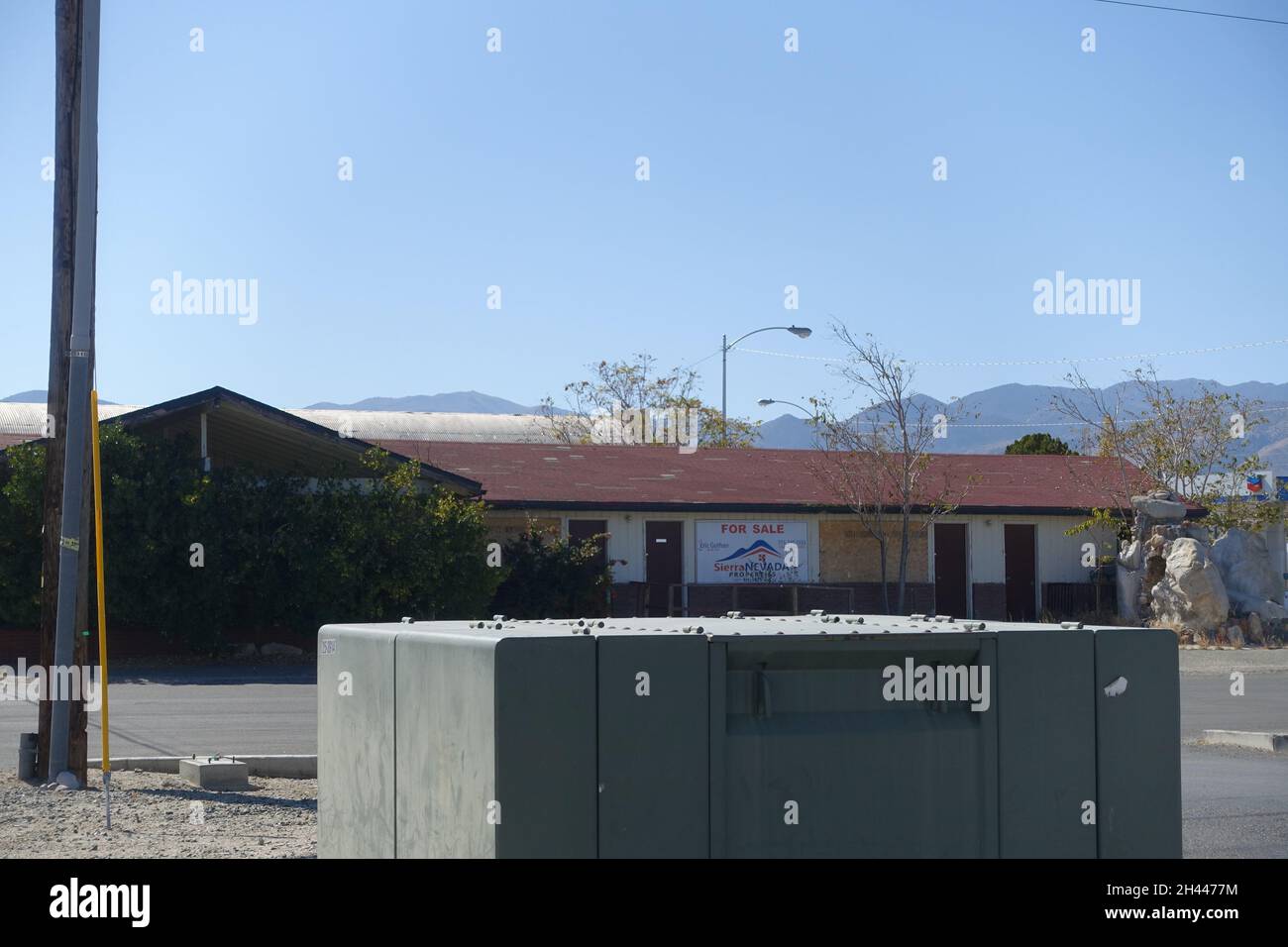Kleiner Versorgungsschuppen oder Servicehaus mit abgeschrägtem Dach und Elektrokasten, Versorgungsmast in der Nähe in offener, trockener Wüstenlandschaft unter klarem blauem Himmel, ru Stockfoto