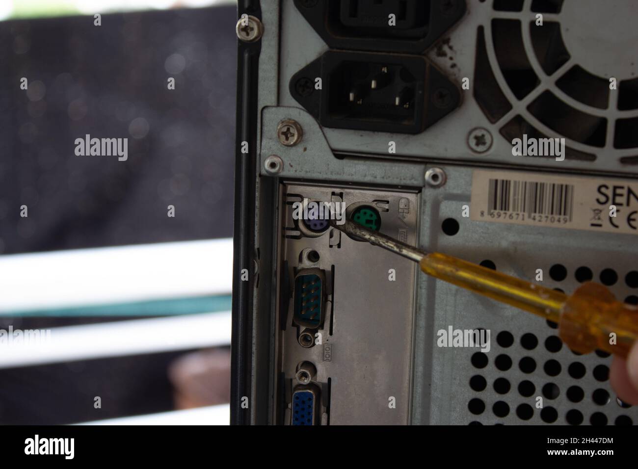 Mit einem gelben, transparenten Schraubendreher auf die hinteren Anschlüsse eines Heimcomputers zeigen. Stockfoto