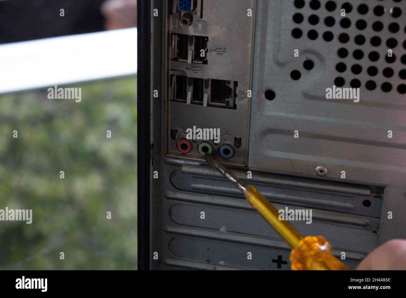 Mit einem gelben, transparenten Schraubendreher auf die hinteren Anschlüsse eines Heimcomputers zeigen. Stockfoto