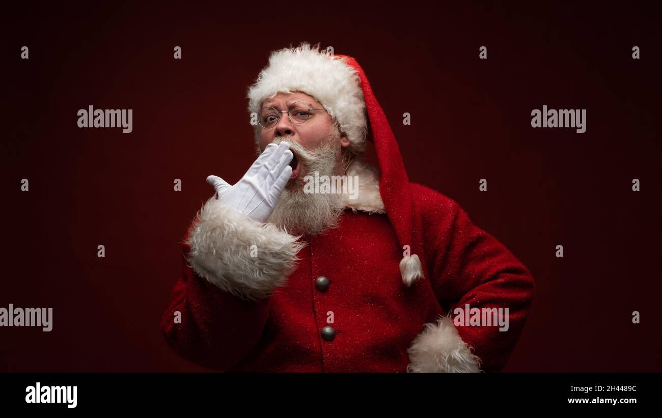 Der Weihnachtsmann gähnt, trägt eine Brille und einen Hut. Stockfoto