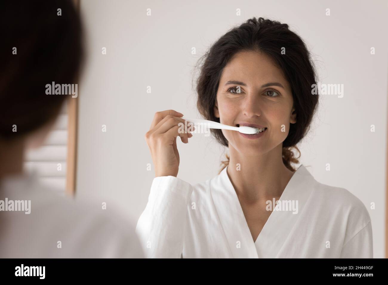 Junge Frau putzt sich die Zähne, die vor dem Spiegel stehen Stockfoto