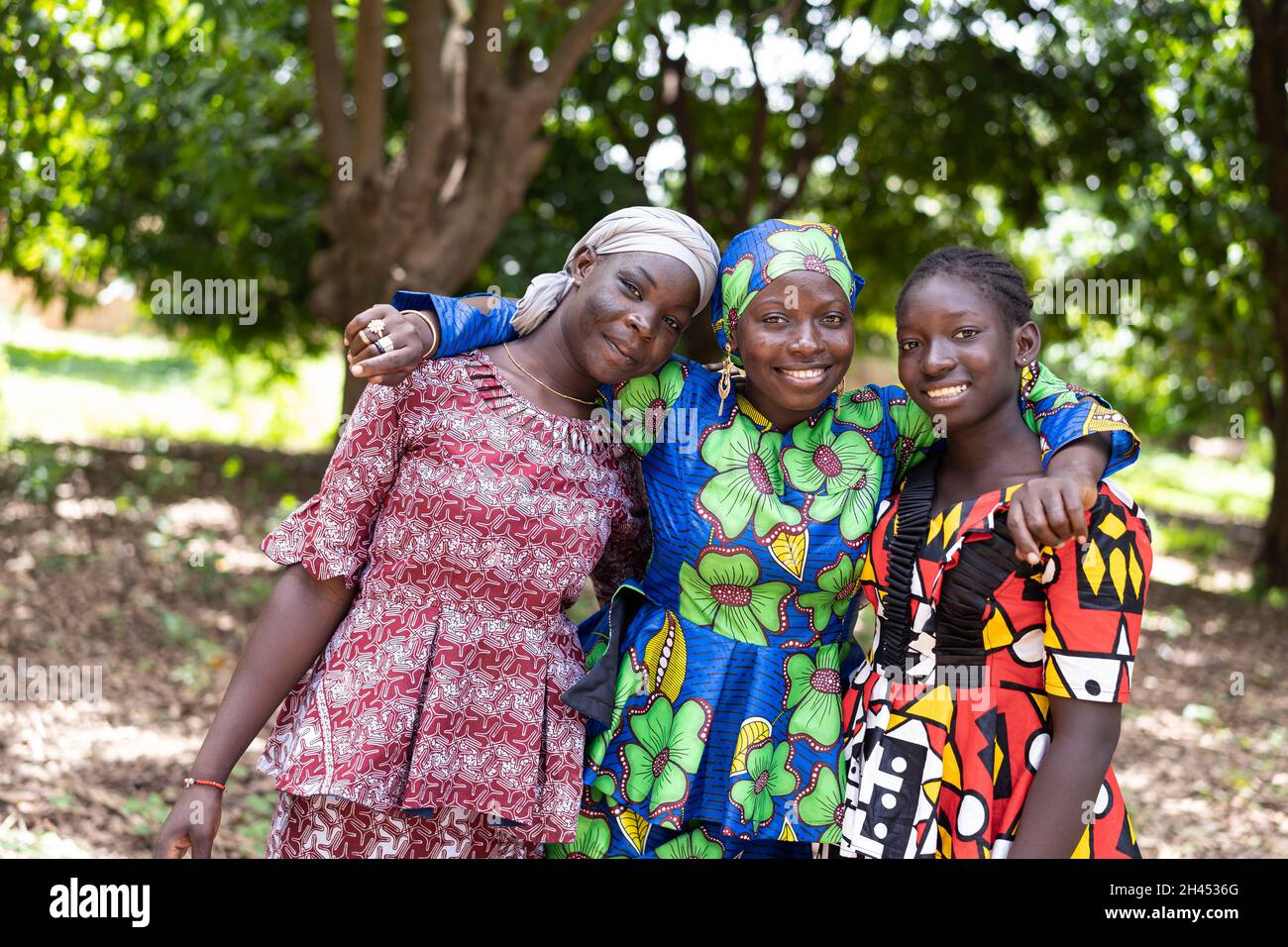 Drei strahlende junge afrikanische Frauen in schönen traditionellen Kleidern, die die Kamera betrachten; Konzept der menschlichen Beziehung Stockfoto