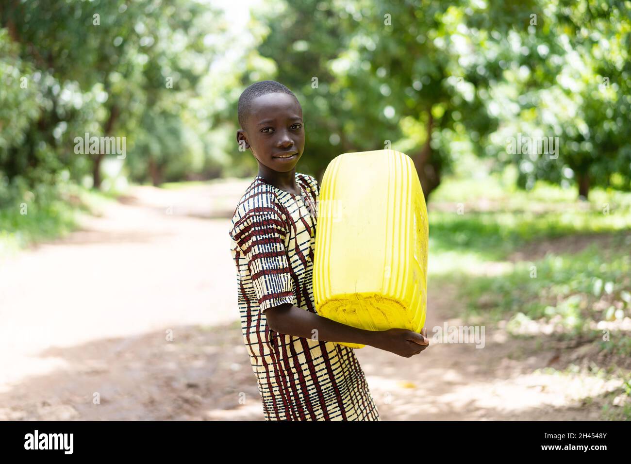 Hübscher kleiner schwarzer afrikanischer Dorfjunge, der einen großen gelben Kanister mit sauberem und frischem Trinkwasser nach Hause trägt; Konzept der Wasserverteilung Stockfoto