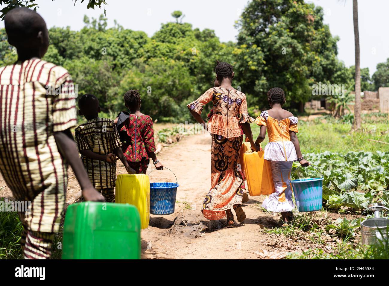 Eine Gruppe von schwarzen Jungen und Mädchen, die Wassertanks irgendwo in einem ländlichen afrikanischen Ackerland tragen Stockfoto