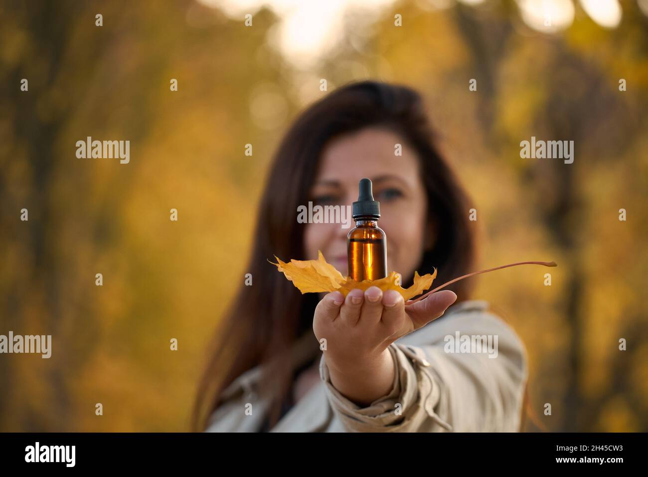 Frau mit einer Flasche mit natürlichem ätherischem Kräuteröl, Herbstklima, gelbe Blätter. Alternative Medizin. Natürliche Ergänzung. Stockfoto