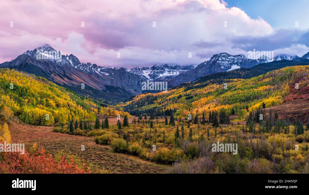 Ein farbenfrohes Tal mit der East Fork des Dallas Creek mit dramatischen Herbstfarben unter Mount Sneffels und stimmungsvollen Sonnenuntergangswolken in den San Juan Mountains. Stockfoto