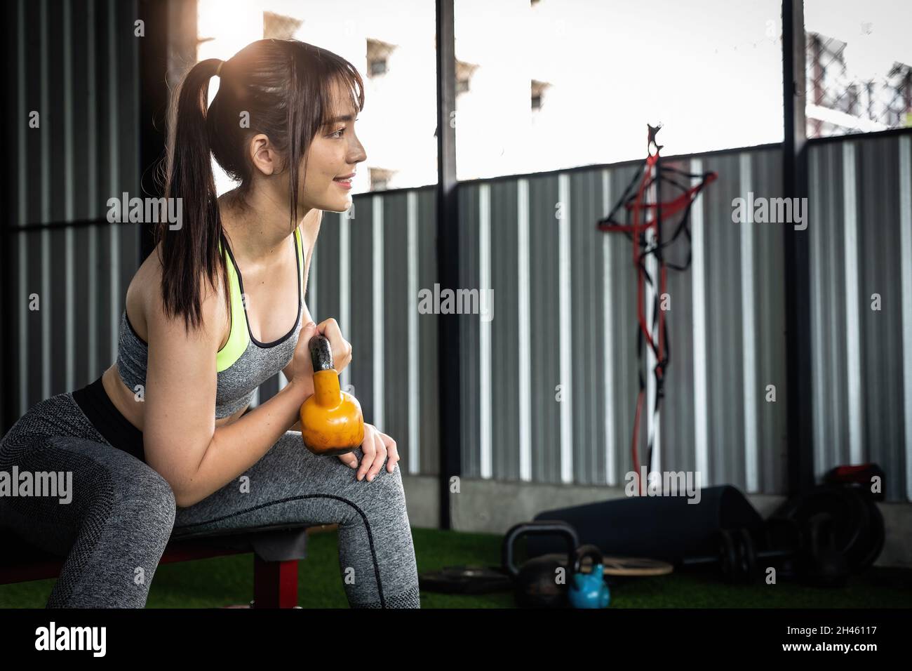 Junge asiatische Frau genießen das Training mit dem Heben Wasserkocher Glocke mit einer Hand in der Turnhalle. Sport Bodybuilding Konzept. Stockfoto