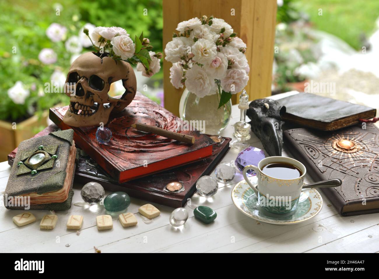 Vintage Sommer Stillleben mit Kristallen, altem Buch, Totenkopf und Rosen auf Hexentisch. Esoterisches, okkultes und mystisches Konzept für Hexerei Stockfoto
