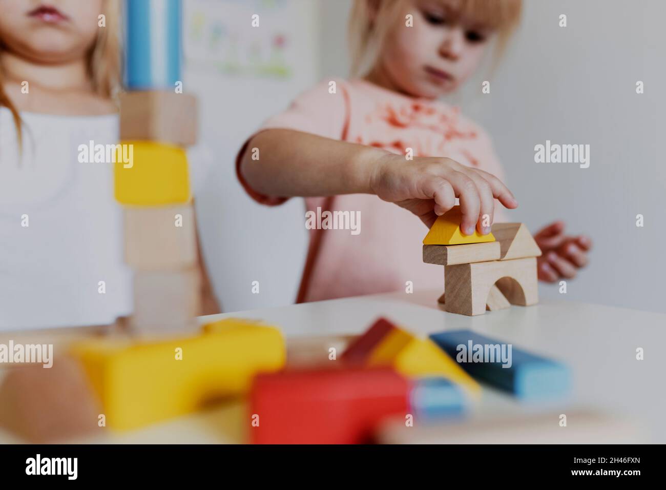 Zwei Mädchen Schwestern spielen mit bunten Holzspielzeug-Bausteinen. Kleines Kind Gebäude Turm oder Haus zu Hause oder Kinderbetreuung. Lernspielzeug für y Stockfoto