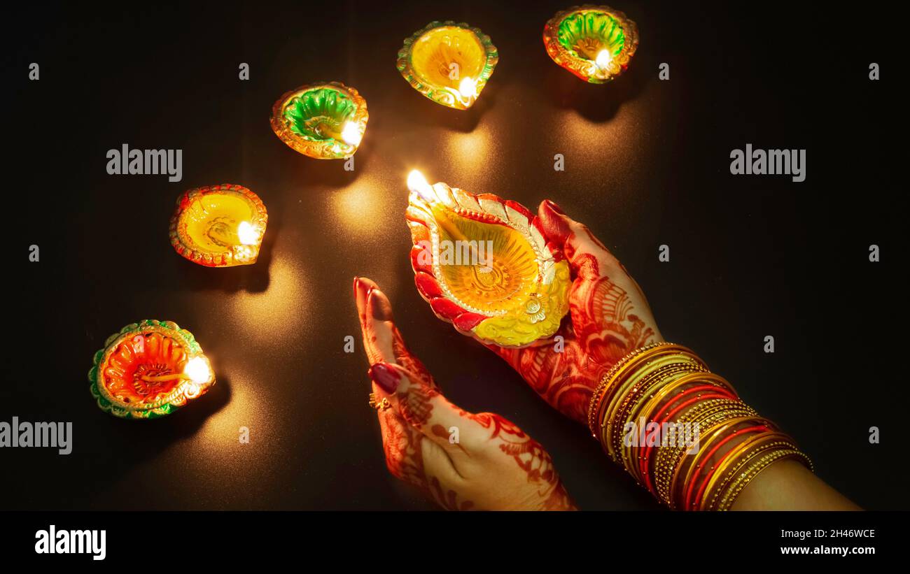 Frau trägt Mehndi und Armreifen, die Diwali Diya-Lampen auf dunklem Hintergrund beleuchten Stockfoto