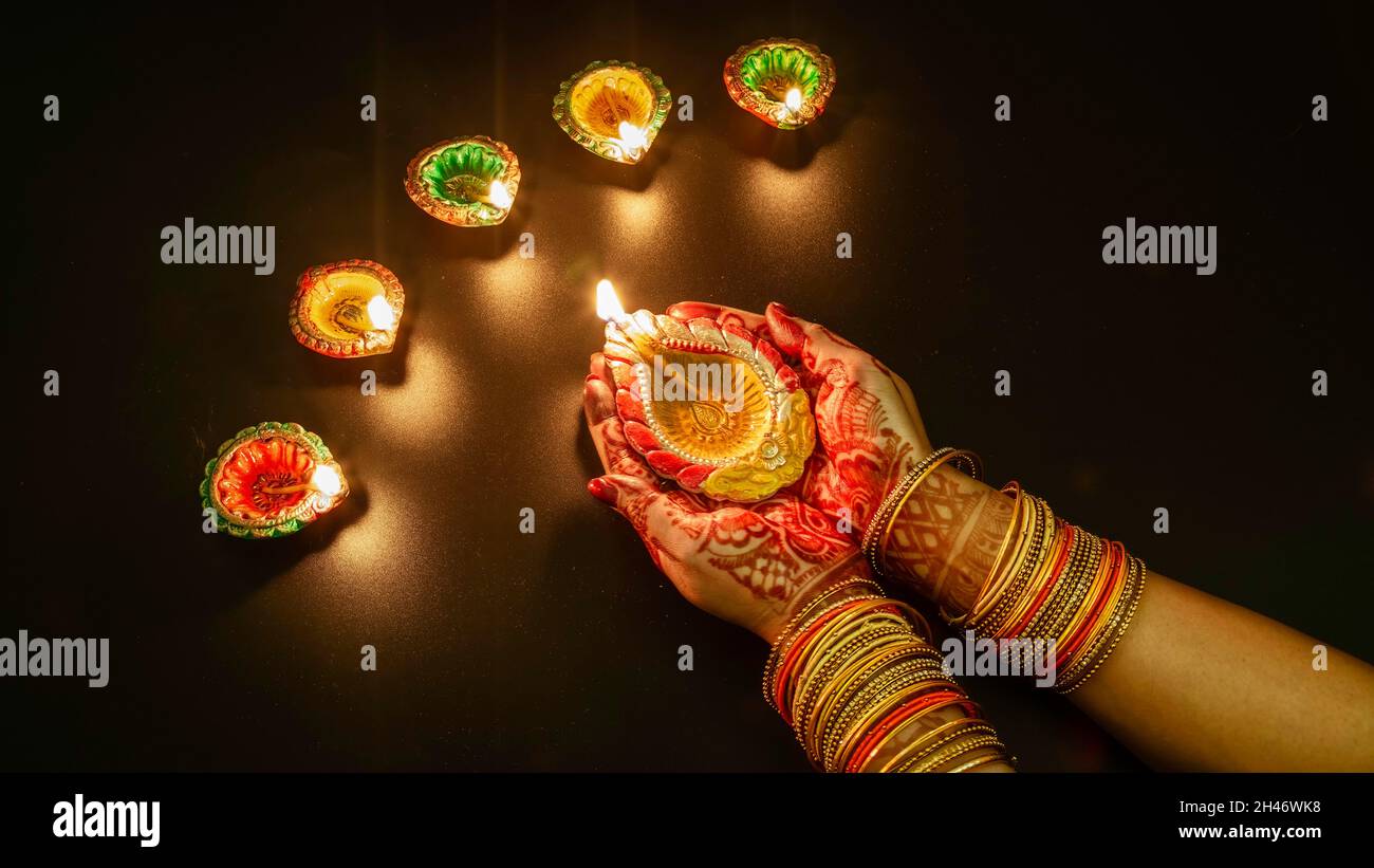 Frau trägt Mehndi und Armreifen, die Diwali Diya-Lampen auf dunklem Hintergrund beleuchten Stockfoto