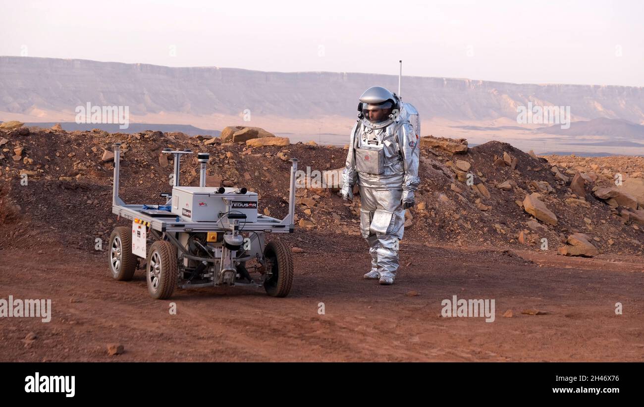 Ein analoger Astronaut, gekleidet in einen speziellen Raumanzügen, umläuft einen Rover auf dem Gelände der Mars-ähnlichen Forschungseinrichtung, die für die AMADEE-20-Mars-Simulation am Ramon-Krater in der Negev-Wüste in Israel gebaut wurde. Sechs Analogastronauten aus Israel, Portugal, Spanien, Deutschland, den Niederlanden und Österreich haben eine dreiwöchige Isolation innerhalb der Forschungseinrichtung abgeschlossen und konnten ihren Lebensraum nur in Raumanzügen verlassen. Das Team führte eine Reihe von wissenschaftlichen und technologischen Experimenten durch, in der Hoffnung, die Grundlagen für zukünftige bemannte Missionen zum Mars zu schaffen. Stockfoto