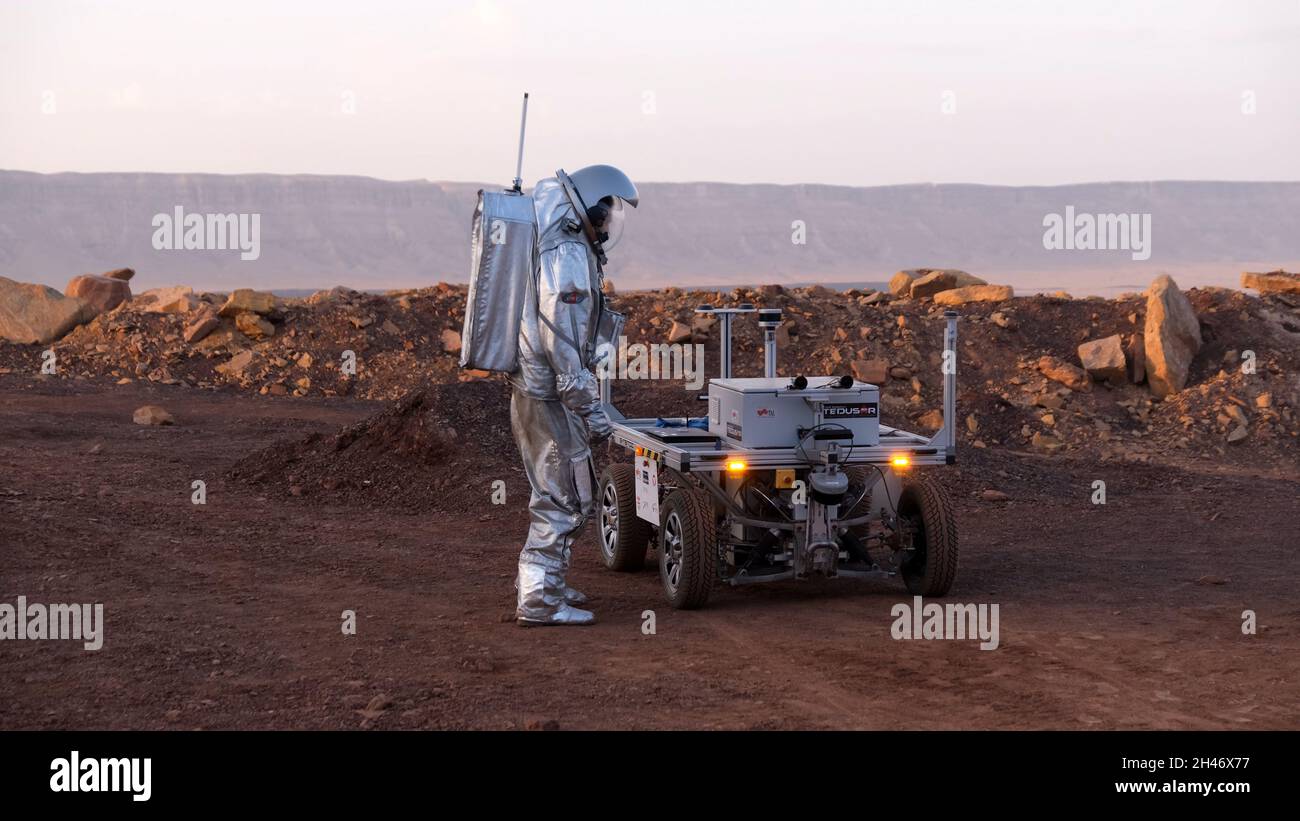 Ein analoger Astronaut, gekleidet in einen speziellen Raumanzügen, umläuft einen Rover auf dem Gelände der Mars-ähnlichen Forschungseinrichtung, die für die AMADEE-20-Mars-Simulation am Ramon-Krater in der Negev-Wüste in Israel gebaut wurde. Sechs Analogastronauten aus Israel, Portugal, Spanien, Deutschland, den Niederlanden und Österreich haben eine dreiwöchige Isolation innerhalb der Forschungseinrichtung abgeschlossen und konnten ihren Lebensraum nur in Raumanzügen verlassen. Das Team führte eine Reihe von wissenschaftlichen und technologischen Experimenten durch, in der Hoffnung, die Grundlagen für zukünftige bemannte Missionen zum Mars zu schaffen. Stockfoto