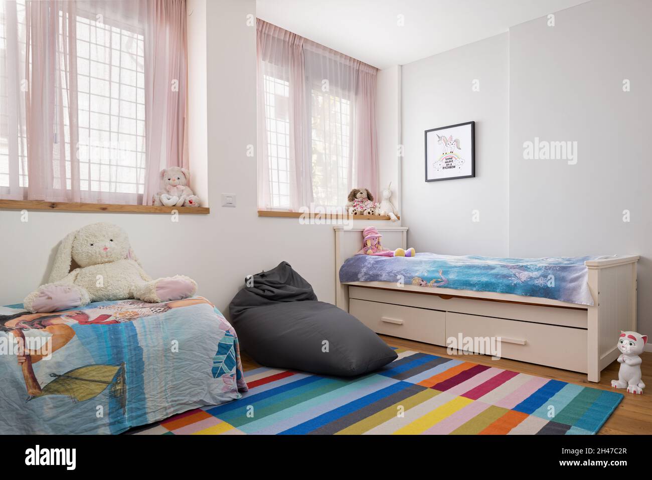 Kinderzimmer mit zwei Betten, rosa Vorhängen, farbenfrohem Teppich, Beanbag-Mütze und Puppen Stockfoto