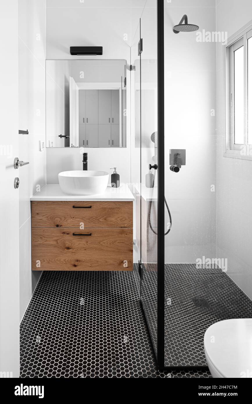 Badezimmer, brauner Holzschrank, beleuchtete Leuchte und abwechslungsreiche Bodenfliesen Stockfoto