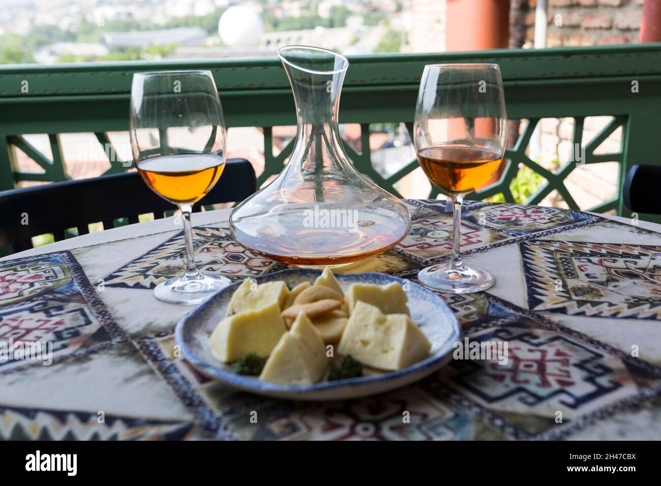 Zwei Gläser und ein Krug, ein Dekanter mit orangefarbenem qvevri-Wein. Ein Teller mit einer Auswahl an georgischen Käsesorten. Tischdecke mit nationalem Ornament. Stockfoto