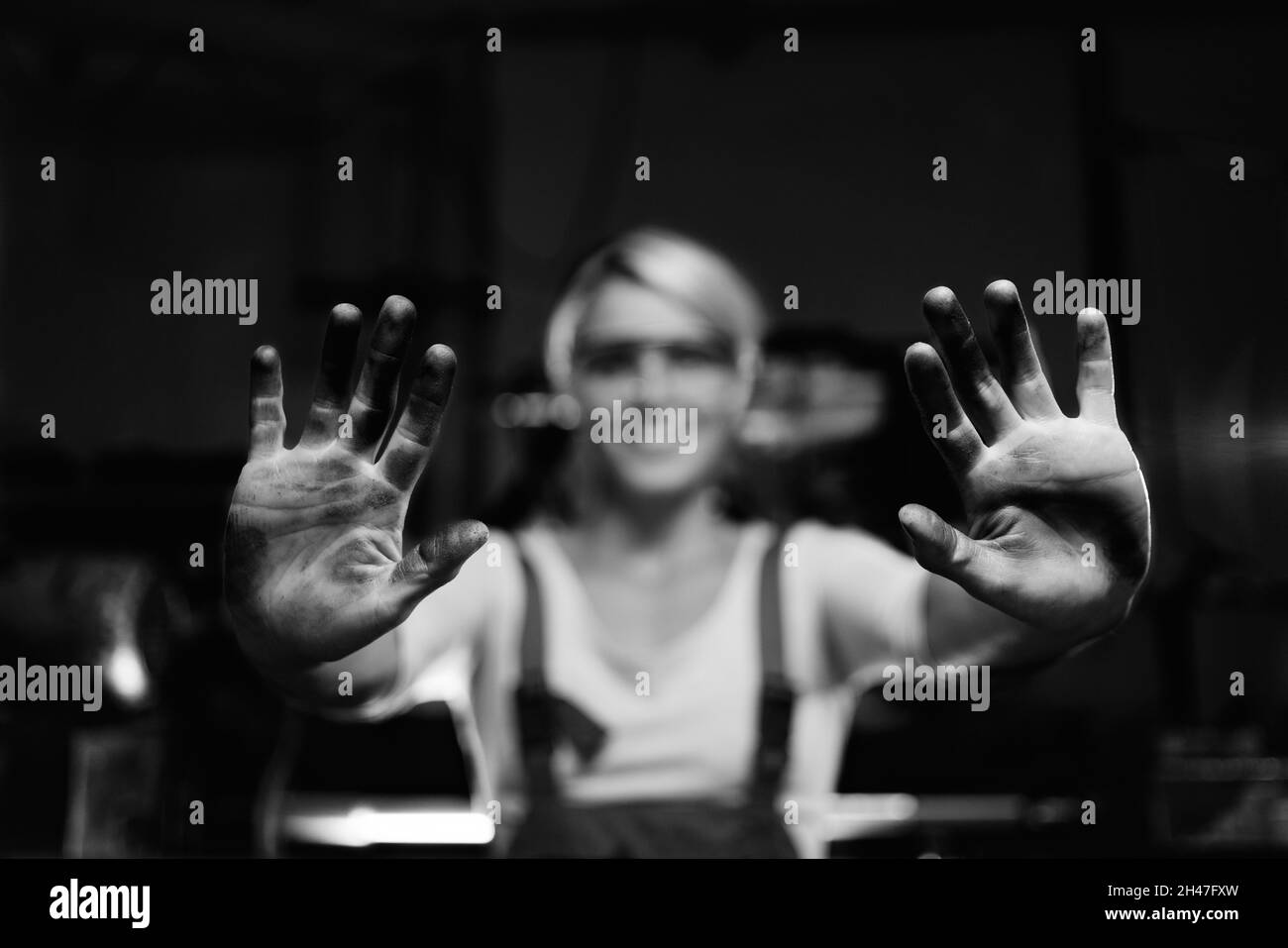 Eine junge Arbeiterin zeigt ihre schmutzigen Hände in Innenräumen in einer Metallwerkstatt Stockfoto