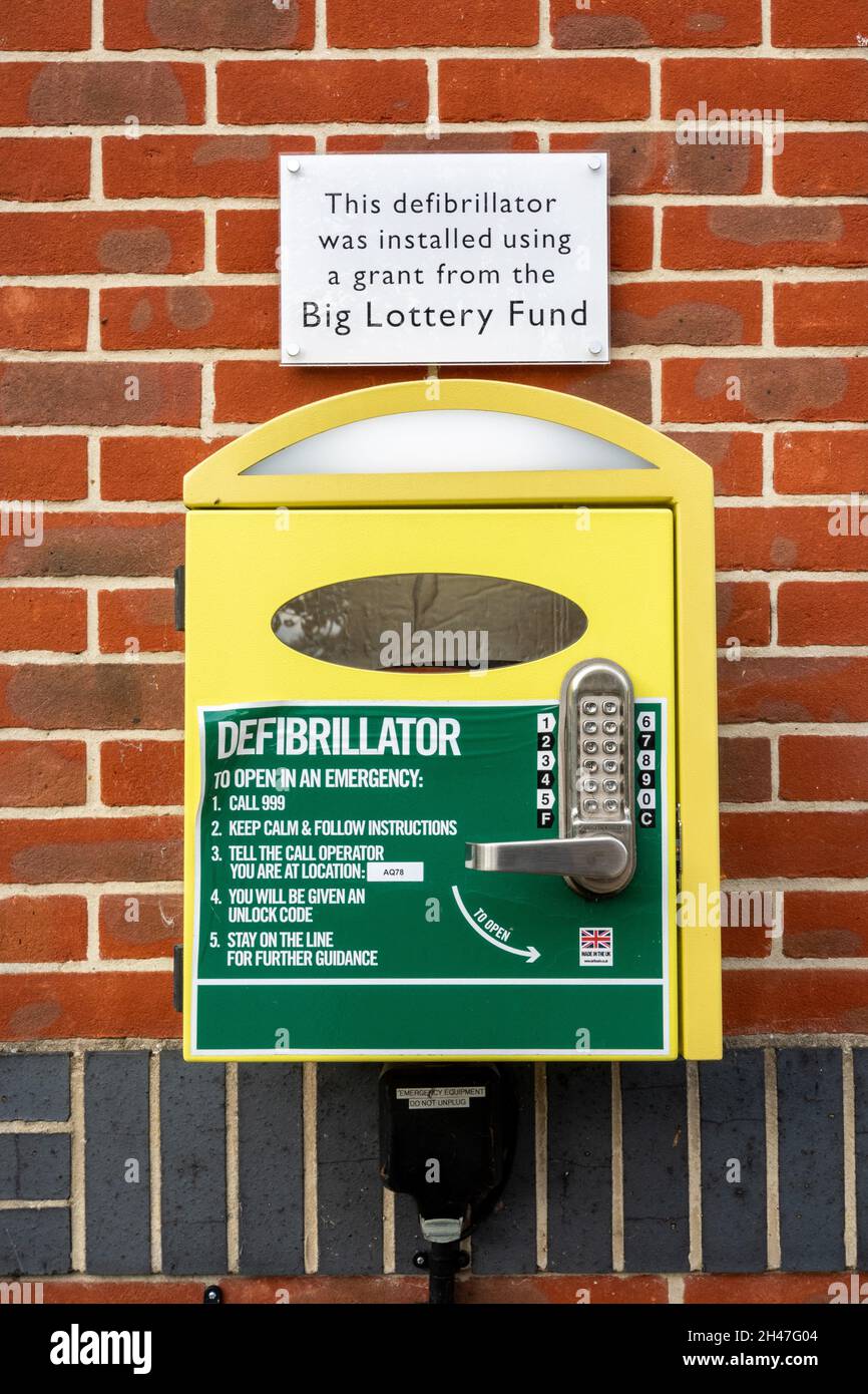 Defibrillator, medizinische Notfallausrüstung in einer Dorfhalle mit einer Tafel, auf der angegeben ist, dass sie vom Big Lottery Fund, Hampshire, England, Großbritannien, finanziert wurde Stockfoto