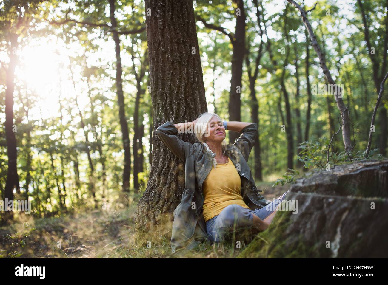 Porträt einer älteren Frau, die sich entspannt und mit geschlossenen Augen im Wald sitzt. Stockfoto