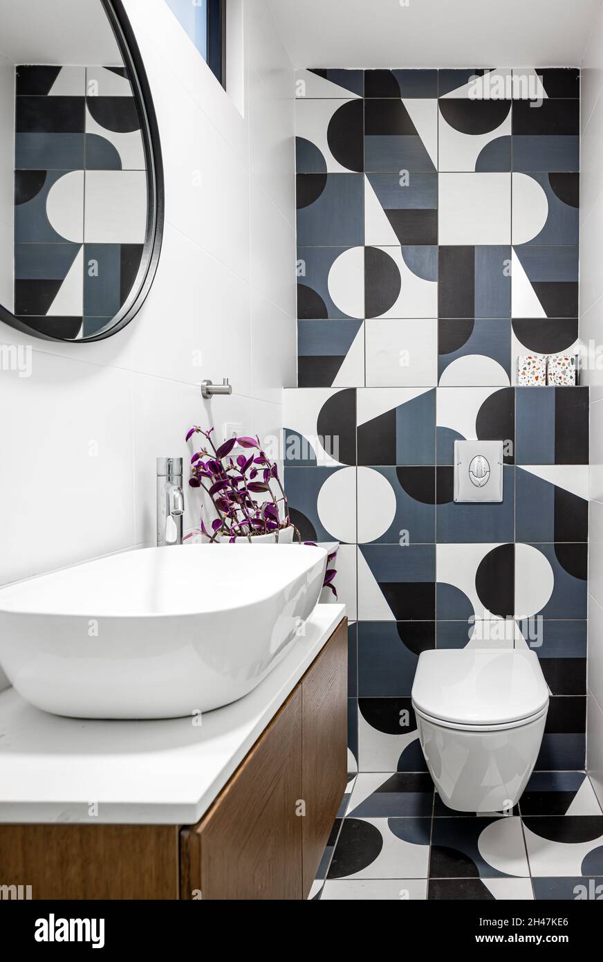 toilette, brauner Holzschrank, runder Spiegel im Waschbecken, beleuchtete Beleuchtungskörper und verschiedene Wand- und Bodenfliesen Stockfoto