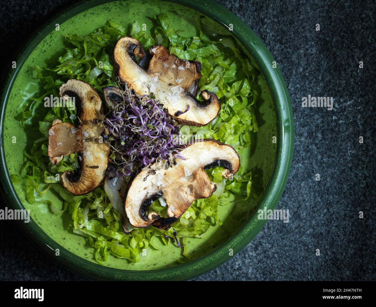 Sautierte portobello-Pilze und Zwiebeln mit violetter Kresse auf einem Salatbett Stockfoto