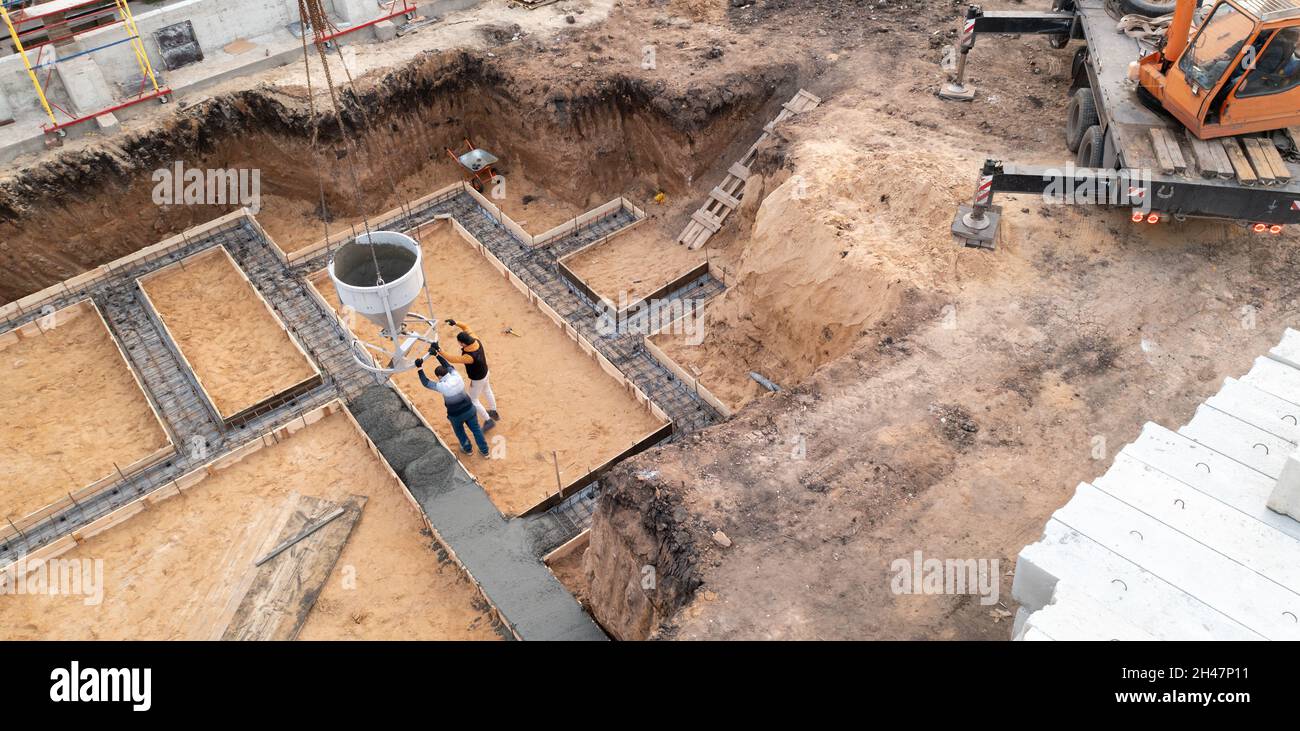 Baustelle mit Arbeitskräften, die Beton in Schalung mit Bewehrung gießen. Feuchter Zement fließt in das Fundament des zivilen Gebäudes, Luftaufnahme. Stockfoto