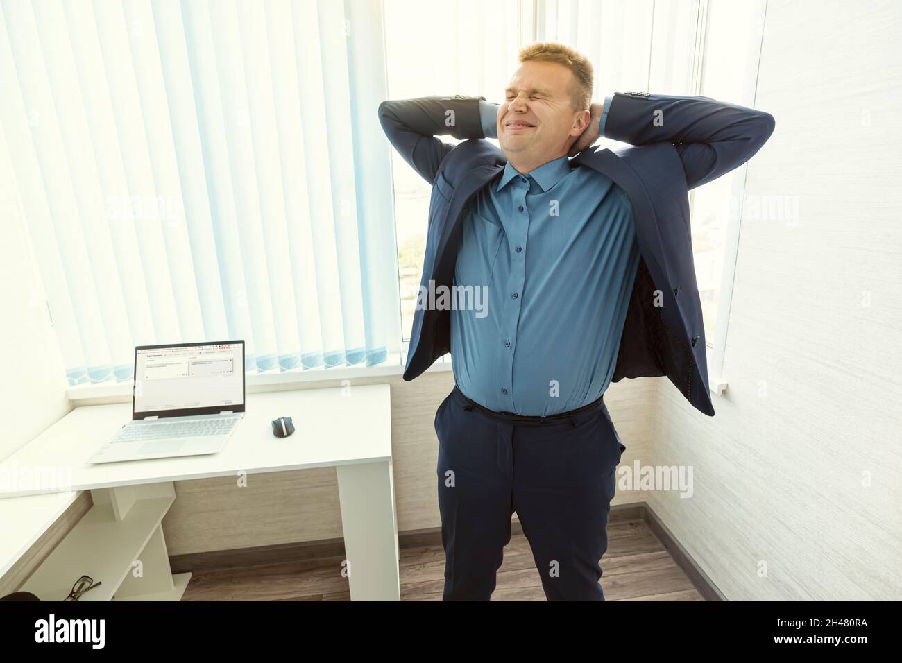 Geschäftsmann, der sich mit einem Laptop am Schreibtisch ausstreckt. Der Manager atmet nach Abschluss der Arbeit tief und entspannt frische Luft ein. Büroangestellter, der sich entspannt Stockfoto