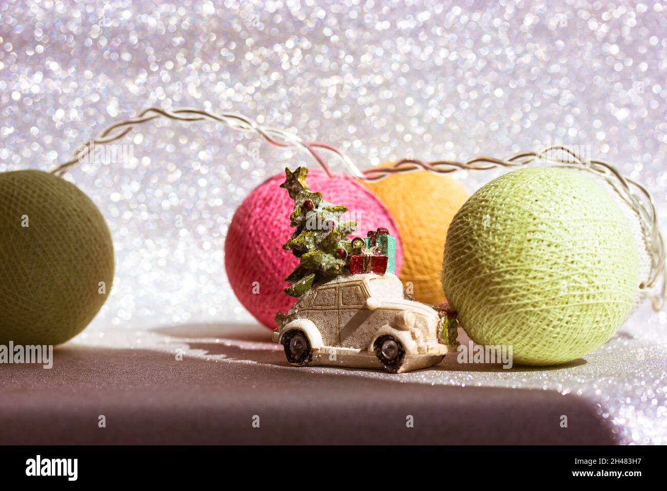 Weißes Spielzeug Retro Auto mit Weihnachtsbaum auf Dach auf versilbertem glänzenden Hintergrund. Grußkarte „Happy New Year's Eve 2022“. Lieferung der Geschenkbox. Garland la Stockfoto