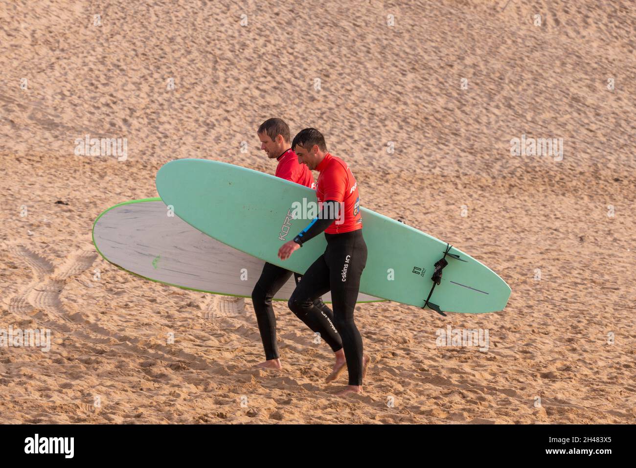 Männliche Surfer geben ihre gemieteten Surfbretter zum Surf-Verleih in Fistral in Newquay in Cornwall zurück. Stockfoto