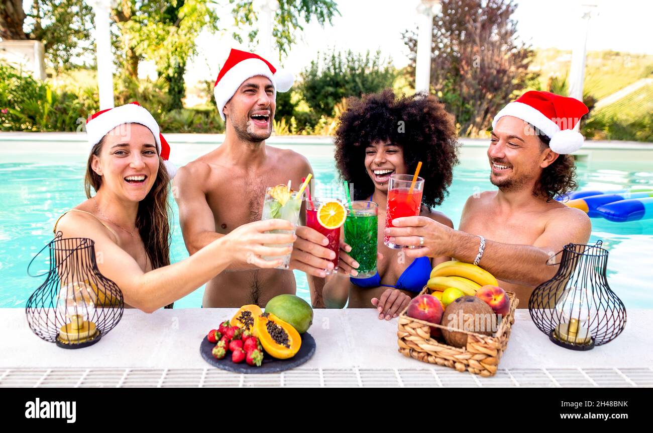 frohe weihnachten! Fröhliche, vielfältige Gruppe von Freunden, die Weihnachtsmütze tragen und Cocktail-Drinks auf der Poolparty genießen, um den Winter zu feiern Stockfoto