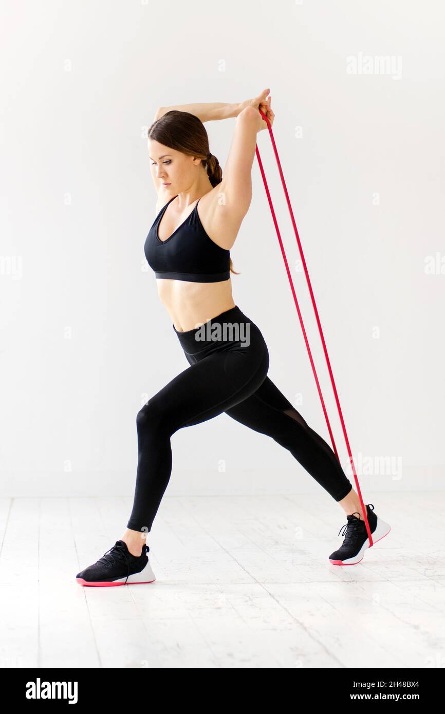 Frau macht Kraftband-Fitnessübungen, um ihre Körpermuskeln über einen hohen Hintergrund in einem Fitnessstudio in einem Gesundheits- und Fitnessconcep zu stärken und zu dehnen Stockfoto