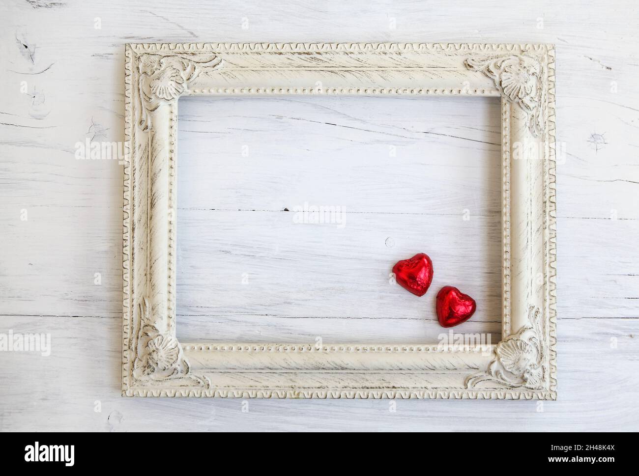 Weißer Holzrahmen mit roten herzförmigen Pralinen Stockfoto