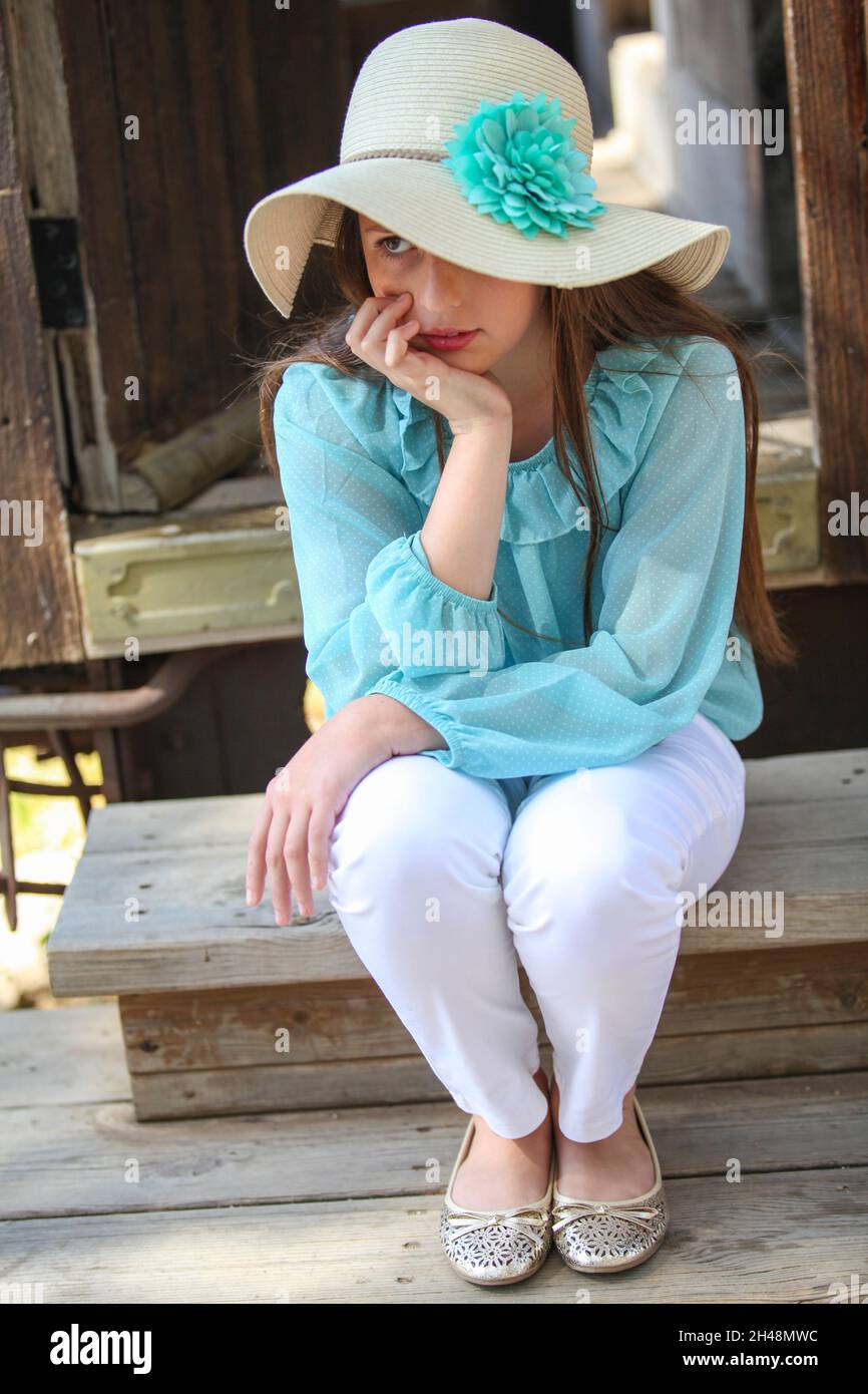 Ein nachdenkliches einsames Mädchen von 11 Jahren in blauer Spitze und Strohhut Stockfoto
