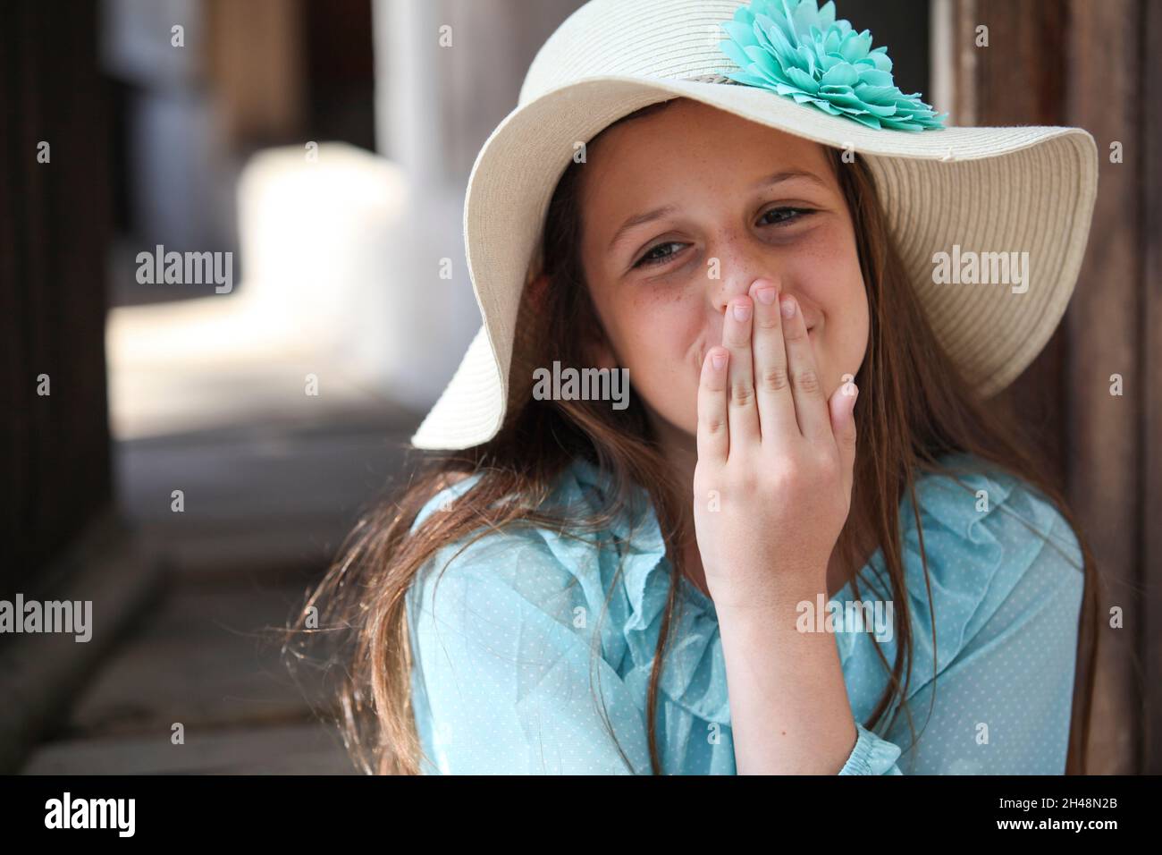 Ein glückliches junges Mädchen von 11 Jahren in blauer Spitze und Strohhut küsst sich Stockfoto