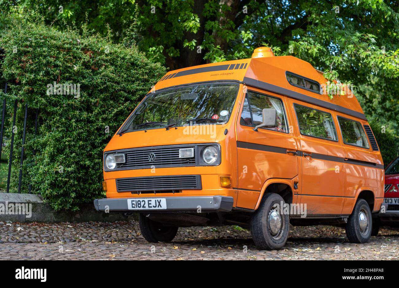 York, Yorkshire, England, 8. Oktober 2021 - Orange Voltswagon T3 Camper Van auf einer Straße mit grünem Laubhintergrund geparkt. Stockfoto