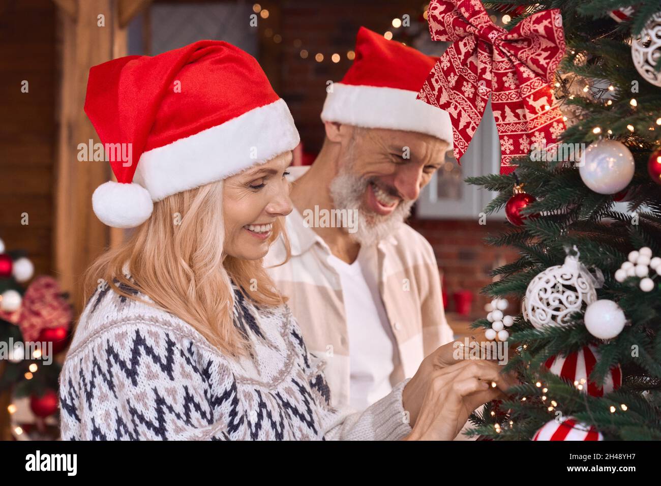 Glückliches reifes altes Paar in den weihnachtsmützen, die Weihnachtsbaum zu Hause dekorieren. Stockfoto