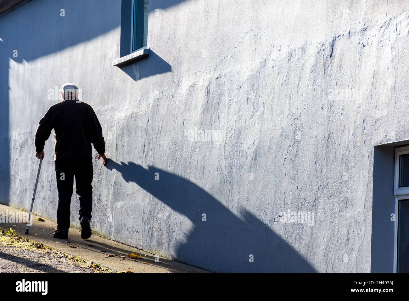 Älterer Mann, der mit Stock und seinem Schatten geht. Stockfoto