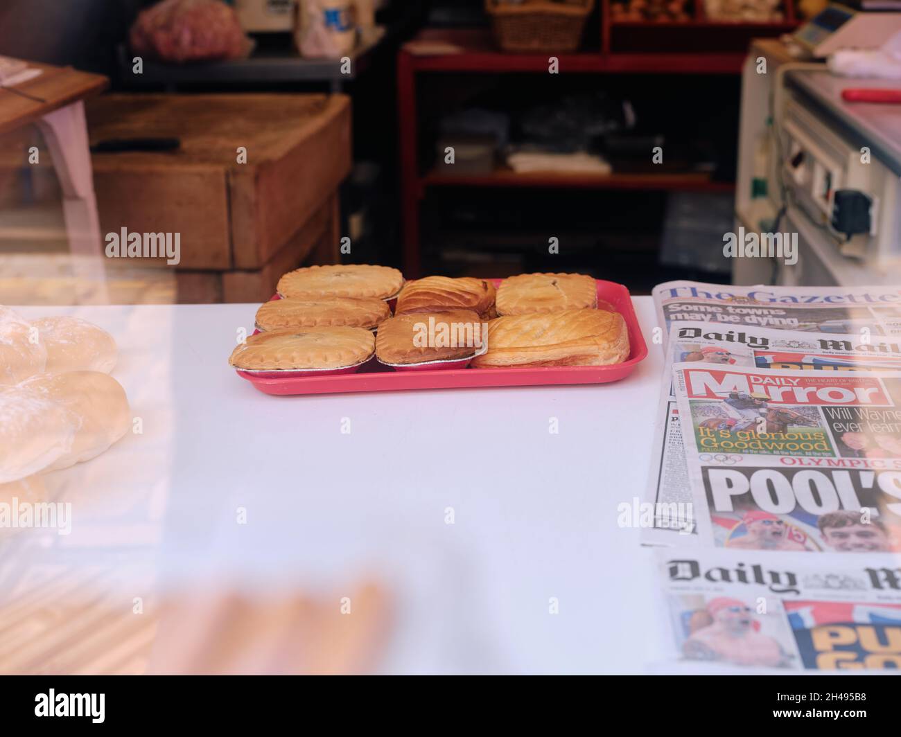 Pies n Papers - britischer Alltag - frisch gebackene Pies und Zeitungen in einer minimalen Schaufenster-Anzeige in Nordengland - Pie Food Zeitung Stockfoto