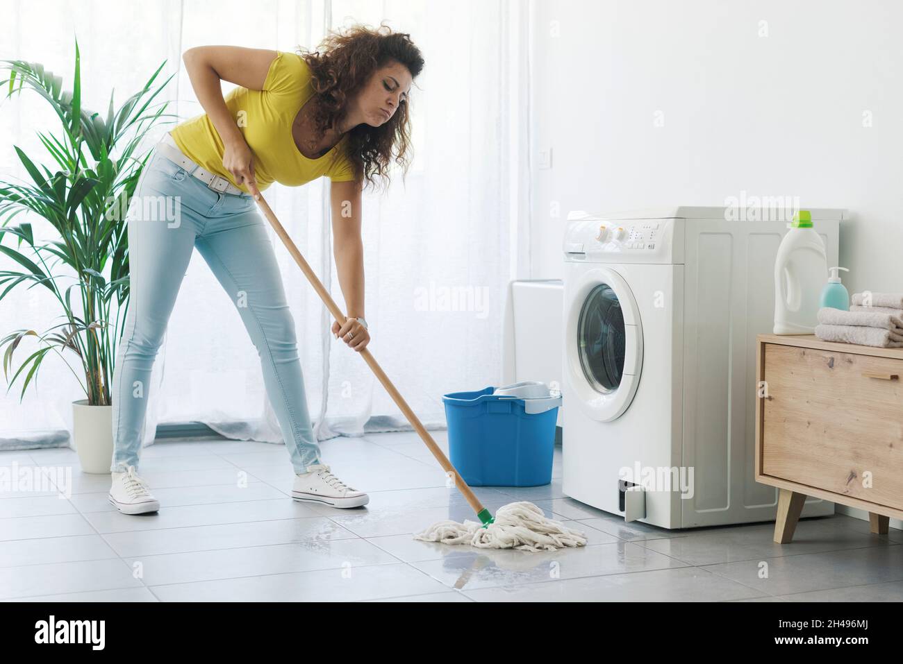 Kaputte Waschmaschine, die Wasser auf den Boden tropfte und enttäuschte die  Frau, die mit einem Wischmopp reinigte Stockfotografie - Alamy