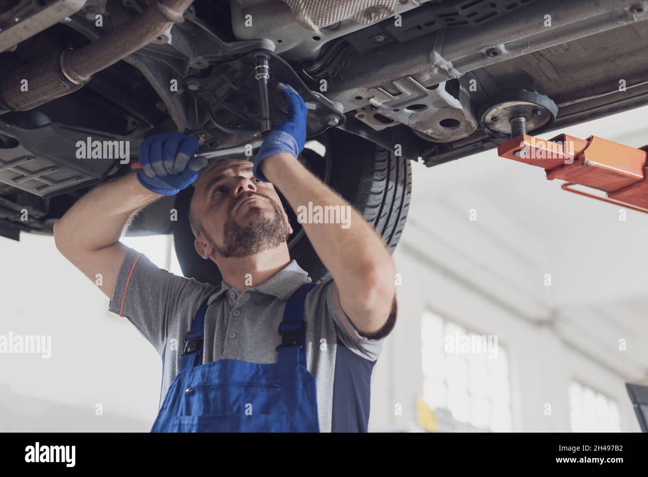 Professioneller Mechaniker, der unter einem Auto arbeitet, führt eine Fahrzeuginspektion durch und prüft auf Undichtigkeiten Stockfoto