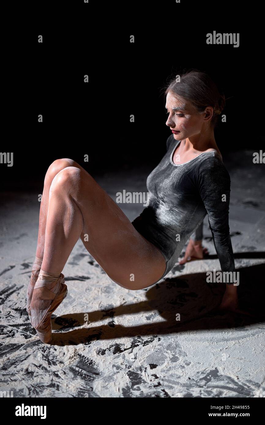 Studioaufnahme, junge anmutige Ballerina. Tänzerin auf Zehen stehend. Seitenansicht Hochformat. Junge Dame im schwarzen Body ruht sich allein aus, macht Pause. Stockfoto