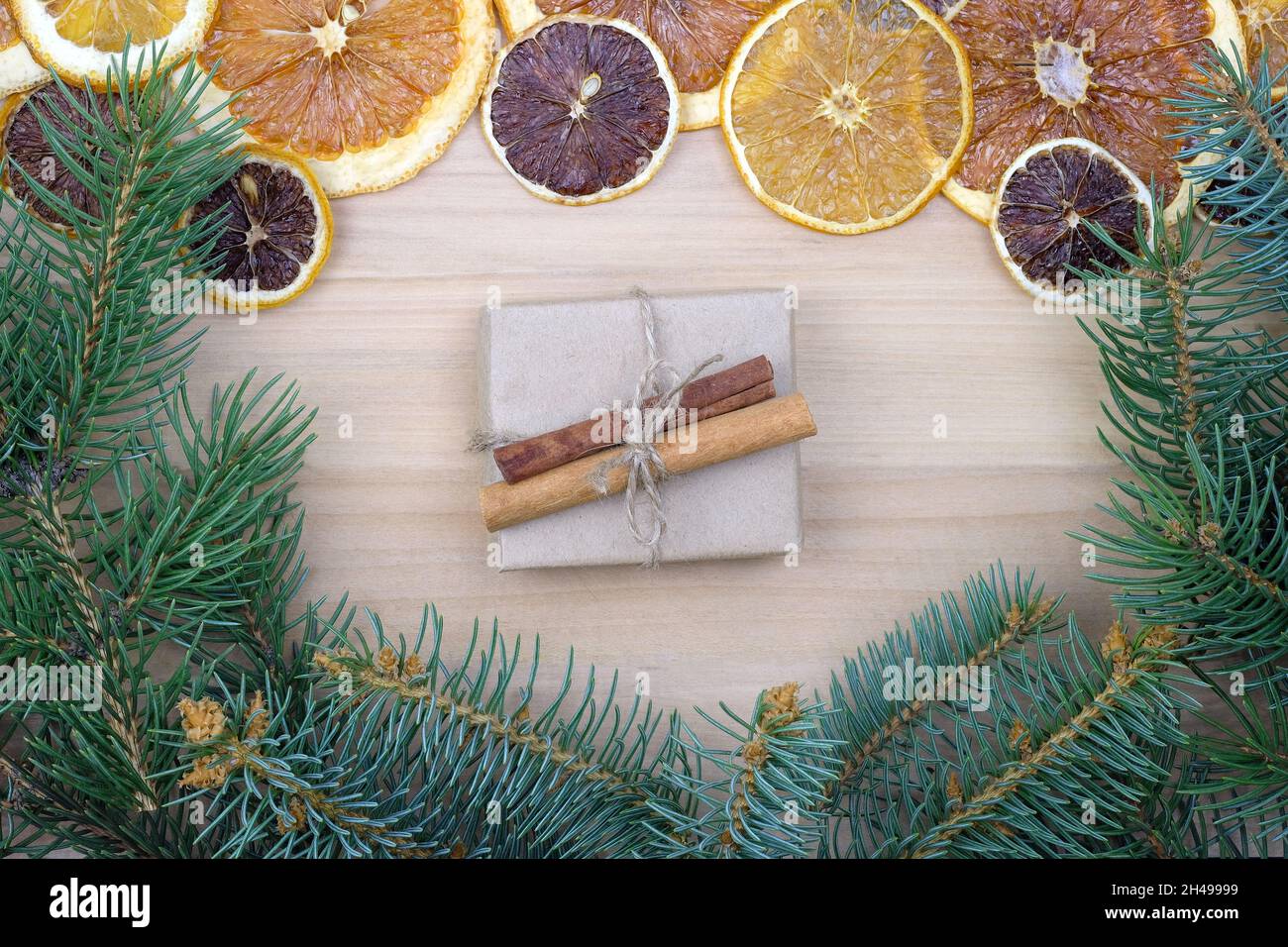 Geschenkschachtel in Bastelpapier mit Zimtstangen verpackt. Weihnachtlicher Hintergrund mit trockenen Orangen, Gewürzen und Zweige eines Weihnachtsbaums. Umweltfreundliches Geschenk Stockfoto