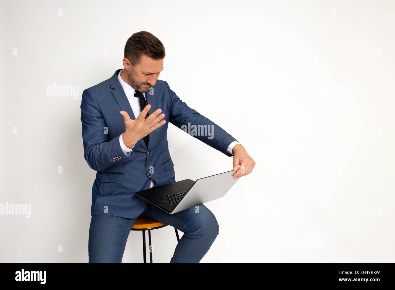 Ein Geschäftsmann, der sich traurig fühlt, und ein Mann, der am Laptop arbeitet. Müde Manager sitzt im Studio auf weißem Hintergrund mit Laptop-Computer müde lo Stockfoto